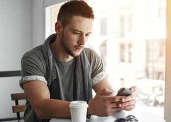 closeup guy sitting table cafe texting message